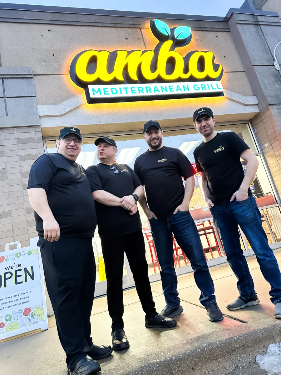 The four brothers who own Amba standing outside the restaurant under the lit Amba sign